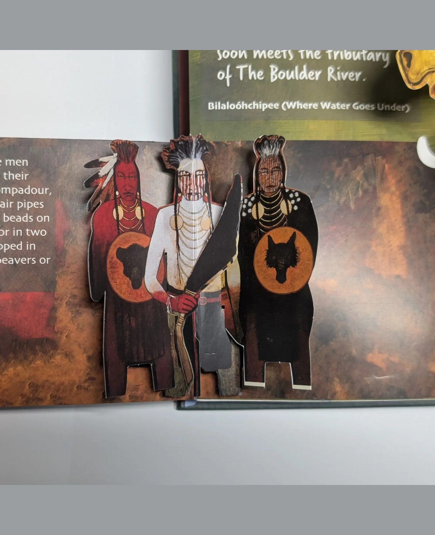 Three individuals in traditional warrior attire holding shields and spears.