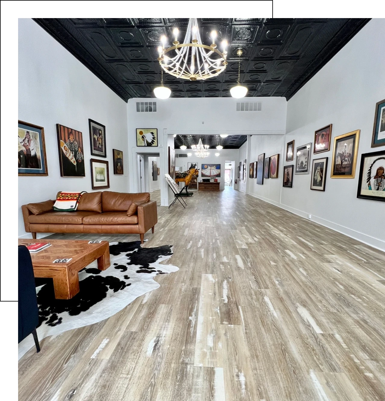 Spacious art gallery with wooden floors and elegant chandeliers.